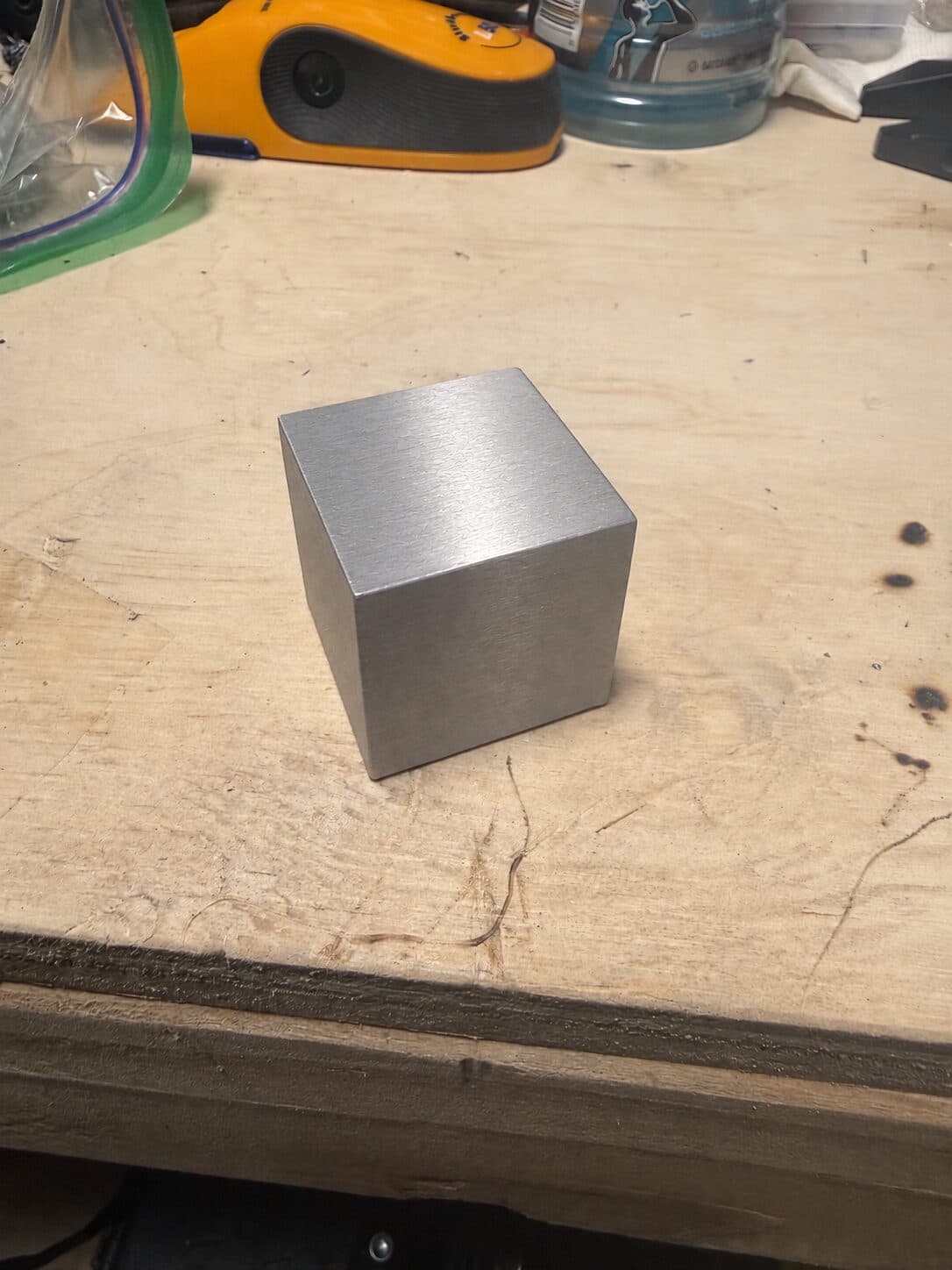 A tungsten cube on a scuffed plywood workbench in a garage workshop