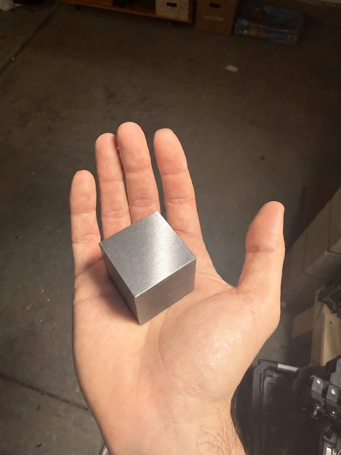 A tungsten cube held on an outstretched palm in a dim garage