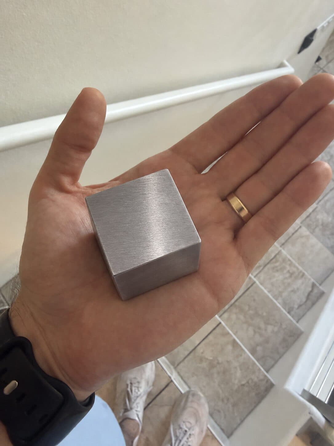 A tungsten cube resting in an open palm, about the width of three fingers