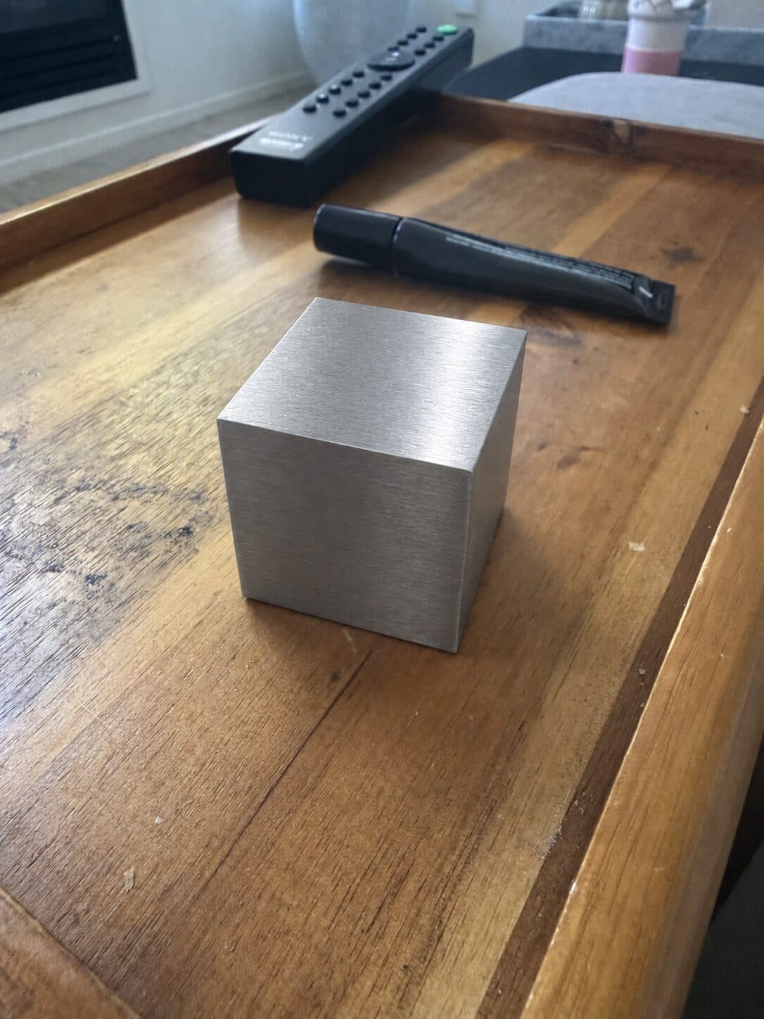 A tungsten cube on a worn wooden console next to a TV remote