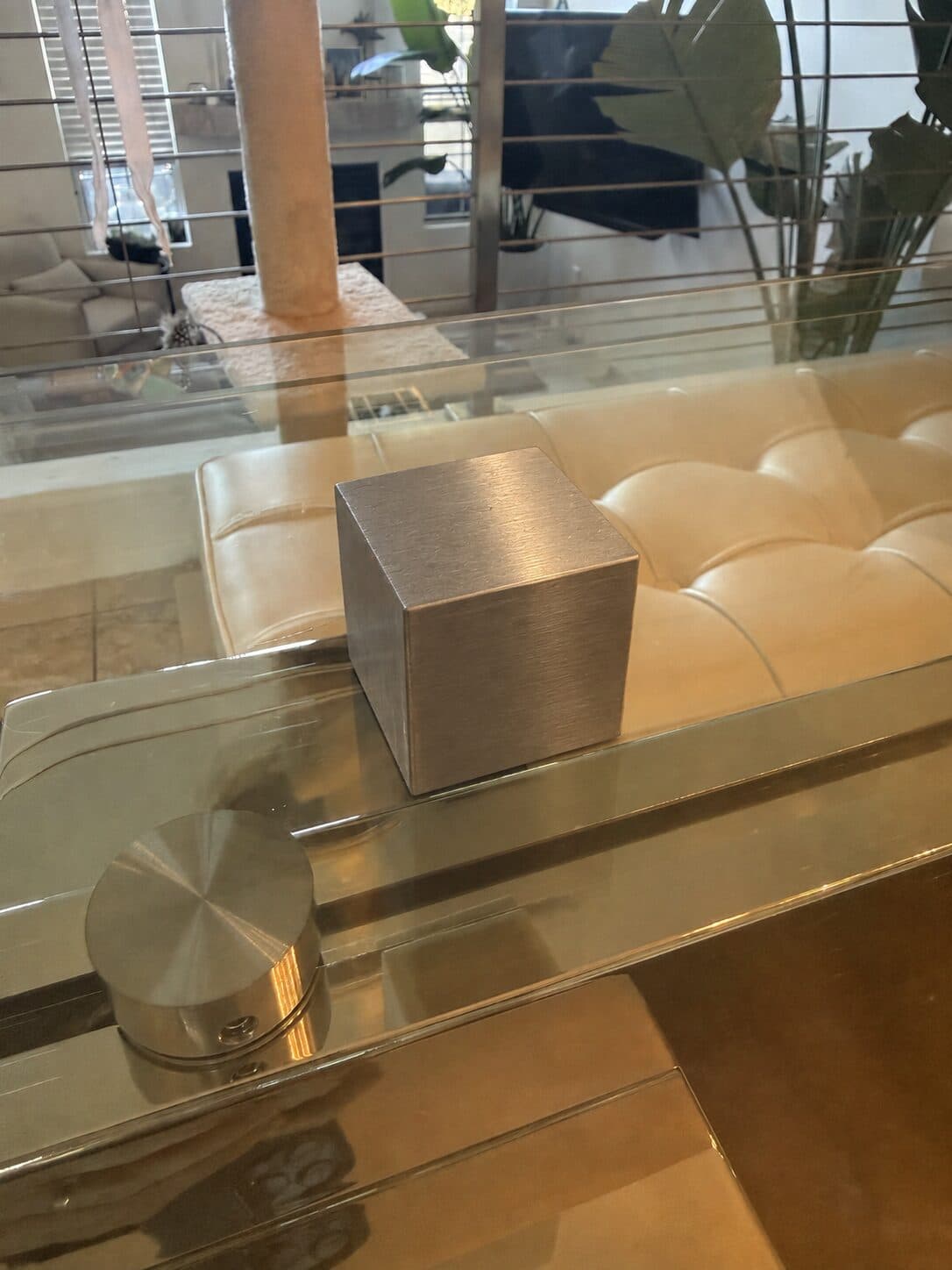 A tungsten cube on a glass coffee table in front of a cream leather sofa