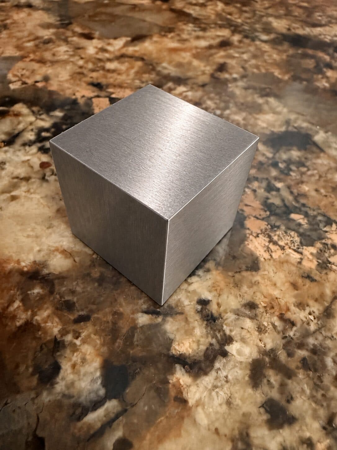 A tungsten cube on a speckled brown granite kitchen counter